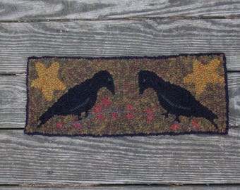May include: A rectangular, hand-hooked rug featuring two black crows facing each other. The rug has a brown background with yellow star-shaped accents and red floral details. The border is dark blue.