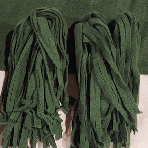 May include: Two bundles of dark green fabric fringe, each about 10 inches long and 3 inches wide.