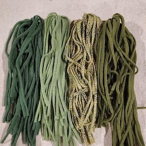 May include: Four bundles of green wool yarn, each with a different shade of green. The yarn is arranged in a row from left to right, with the darkest green on the left and the lightest green on the right.
