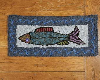 May include: A blue, green, red, and purple fish rug with a white background and a blue border. The rug is made of yarn and has a textured surface.