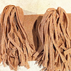 May include: Two bundles of tan and white checkered fabric strips arranged on a rectangular piece of matching checkered fabric. The strips are long, thin, and hang vertically, displaying a consistent waffle-like texture throughout the material.