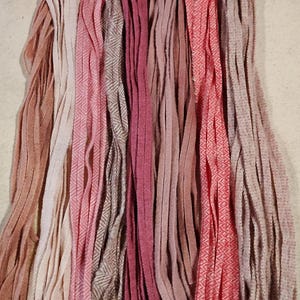 May include: A collection of pink, red, and brown yarn strands with different textures, including plain, herringbone, and striped patterns.