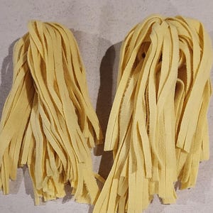May include: Two bundles of yellow fabric fringe, each about 10 inches long and 4 inches wide. The fringe is made of thin, soft fabric strips that are tied together at the top.