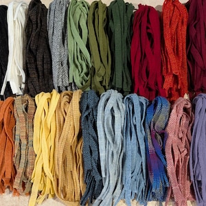 May include: A collection of fabric strips arranged in two rows, featuring a variety of solid colours and herringbone patterns. The assortment includes black, white, brown, grey, green, red, burgundy, orange, yellow, blue, pink, and purple tones.