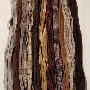 May include: A collection of wool fabric strips in various shades of brown, beige, and gray. The strips are arranged vertically and have different textures and patterns, including plaid and herringbone.