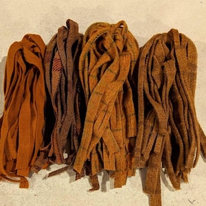 May include: Four bundles of fabric strips in shades of brown and orange. The strips are arranged in a loose, gathered fashion, with varying textures and patterns. The colors range from a deep rust to a lighter, golden-brown.