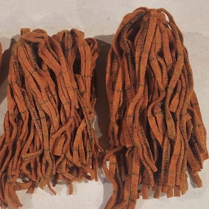 May include: A bundle of orange and brown wool yarn with a plaid pattern. The yarn is cut into long strands and is ready to be used for crafting.