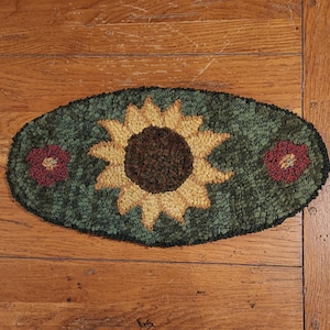 Può includere: Un tappeto ovale verde con un girasole giallo al centro e due fiori rossi su entrambi i lati.