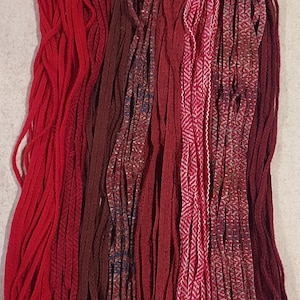 May include: A collection of red, burgundy, and pink yarn strands. The yarn is arranged in vertical rows, creating a colorful and textured display.