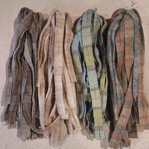 May include: Four bundles of fringed fabric strips in various colours. The colours include shades of brown, beige, and green, with plaid and tweed patterns. The strips are arranged side by side, showcasing the different textures and designs.