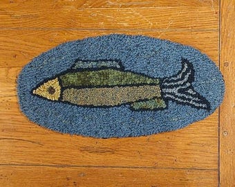 May include: A blue and green fish rug with a yellow eye, on a wooden surface.