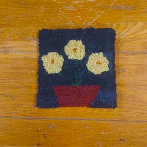 May include: A hand-stitched rug with a dark blue background featuring three yellow flowers in a red pot.