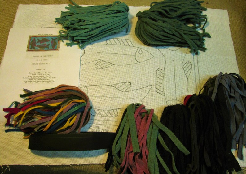 May include: A needlepoint kit featuring a design of three fish with a black outline on white canvas. The kit includes a variety of colored felt strips for embroidery, a black felt strip, and instructions.