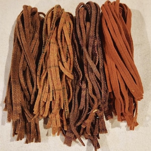 May include: Four bundles of flat, flexible strips arranged side by side. The strips are in varying shades of brown, including dark chocolate, tan, deep mahogany, and a vibrant rust orange, all featuring a soft, matte, and fibrous texture.