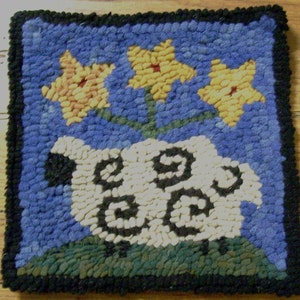 May include: Hand-hooked square rug featuring a sheep design with three yellow flowers. The sheep is white with black accents, set against a blue background with a black border. The rug is approximately 30 cm square.