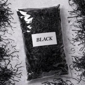 May include: A clear plastic bag filled with black shredded paper, with the word "BLACK" on a white label. The shredded paper is scattered around the bag on a gray surface.