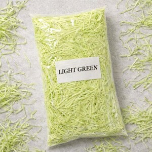 May include: A clear plastic bag filled with light green shredded paper. A white label on the bag reads "LIGHT GREEN". The shredded paper is scattered around the bag on a gray surface.