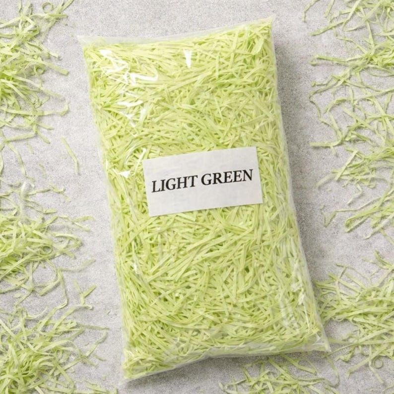 May include: A clear plastic bag filled with light green shredded paper. A white label on the bag reads "LIGHT GREEN". The shredded paper is scattered around the bag on a gray surface.