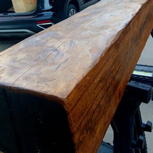 May include: A large, rustic wooden beam with a dark brown stain and a natural wood grain. The beam is thick and has a slightly rounded edge. It is likely made from reclaimed wood and would be a great addition to a farmhouse or rustic decor style.