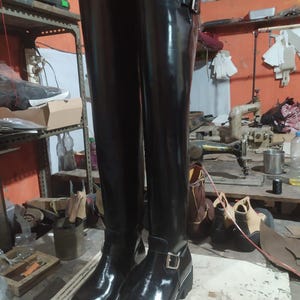 May include: A pair of black leather knee-high boots with silver buckles and a chunky sole. The boots have a shiny finish, reflecting the light. The boots are designed for both style and durability, with a classic design.