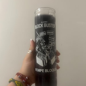 May include: A black candle with white text that reads "Alleged Block Buster" and "Rompe Bloque". The candle has a graphic of a lightning bolt breaking through a wall with text that reads "Fast Luck", "Money Drawing", "Commanding", "Success", "Follow Me", and "Love Me".