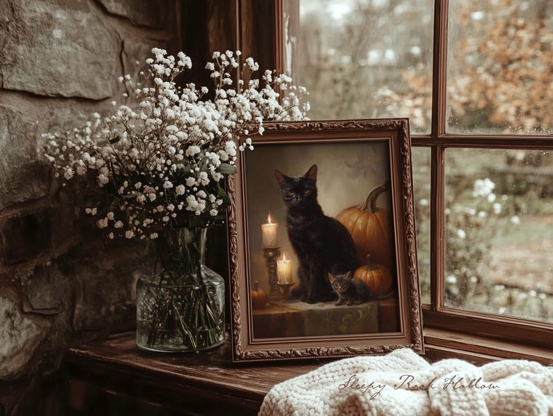 May include: A framed painting of a black cat with a kitten and pumpkins, lit by candles. The painting is on a wooden surface, next to a vase of white flowers. The text "Sleepy Reed Hollow" is visible on a blanket.