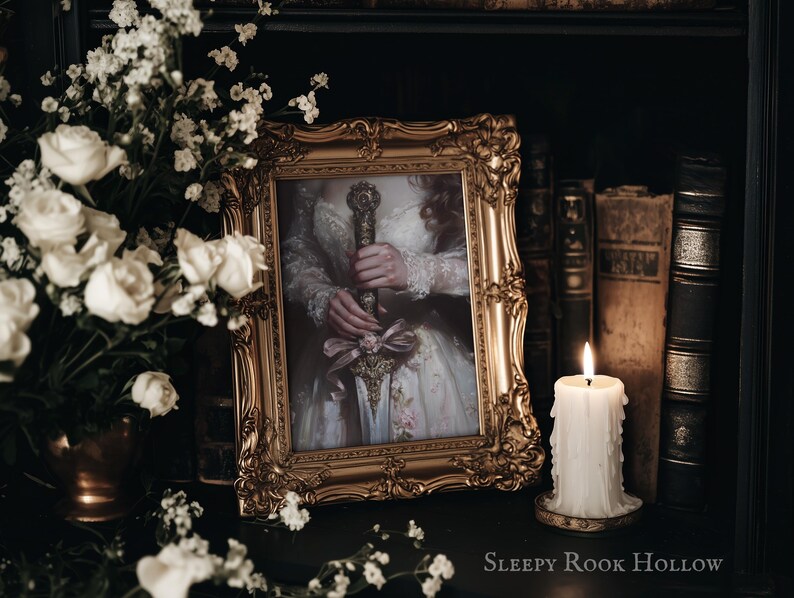 May include: A framed portrait of a woman in a white dress holding a sword. The frame is gold and ornate. The portrait is set on a shelf with books and a candle.