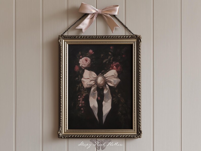 May include: A framed artwork featuring a large white bow with a cameo in the center, surrounded by roses and foliage. The artwork is in an ornate gold frame and is suspended by a chain. A matching pink bow is tied above the frame.