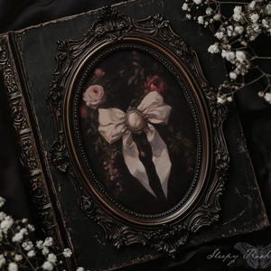 May include: An antique-style framed oval print featuring a bow with a pearl-like center, roses, and a dark background. The frame is ornate and dark, resting on a dark green, aged book. White flowers are in the foreground.