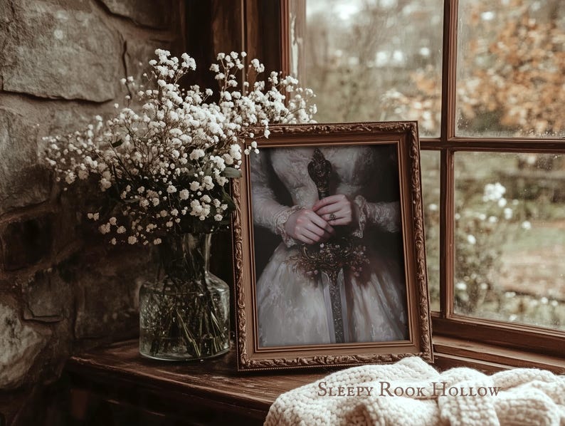 K&ouml;nnte beinhalten: Ein gerahmtes Portr&auml;t einer Frau in einem wei&szlig;en Kleid, die einen Blumenstrau&szlig; h&auml;lt. Das Portr&auml;t ist in einem goldenen Rahmen und steht auf einer Holzoberfl&auml;che. Der Text "SLEEPY ROOK HOLLOW" ist unterhalb des Rahmens sichtbar.