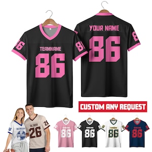 May include: Black football jersey with pink accents, featuring the number 86 in pink. The front displays "TEAMNAME" and the number 86. The back has "YOUR NAME" and the number 86. Additional jerseys in various colors are also shown.