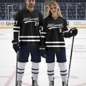 May include: Two people wearing black hockey jerseys with white stripes and the text "86Concept". The jerseys have the numbers 27 and 9. They are wearing navy shorts, white socks with blue stripes, and black hockey skates, holding hockey sticks.
