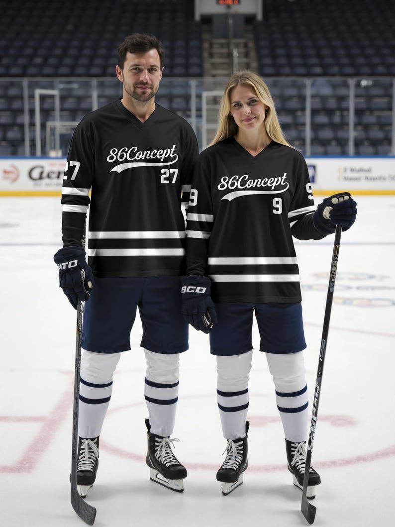 May include: Two people wearing black hockey jerseys with white stripes and the text "86Concept". The jerseys have the numbers 27 and 9. They are wearing navy shorts, white socks with blue stripes, and black hockey skates, holding hockey sticks.
