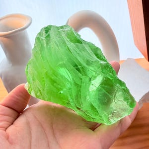 Può includere: Un grande pezzo di vetro traslucido di un vibrante verde lime, con una forma irregolare e frastagliata e una superficie liscia e riflettente. L'oggetto presenta bolle interne e bordi affilati e angolari, mostrando un colore verde vivido.