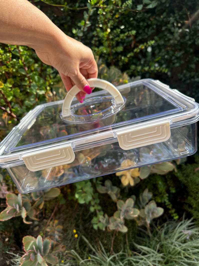 Puede incluir: Un recipiente de almacenamiento de pl&aacute;stico transparente con una tapa blanca y un asa blanca. El recipiente tiene una forma rectangular y est&aacute; hecho de pl&aacute;stico duradero.