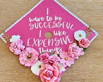 Adorno para birrete de graduación con purpurina rosa y cita personalizada con detalles florales.