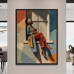 May include: A framed art print depicts a person seated on a windowsill, holding a glass of red wine. The person wears a headscarf, blue jacket, and rust-colored pants. The background features abstract shapes in orange, blue, and beige.