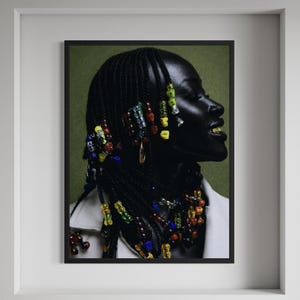 May include: A framed portrait of a person with dark skin and intricately styled black braids adorned with colorful beads. The person is wearing a white jacket and gold teeth. The background is a muted green.