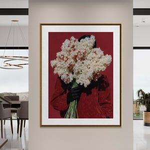 May include: A framed art print featuring a person holding a large bouquet of white and brown flowers against a red background. The person is wearing a red jacket and black gloves. The artwork is displayed in a modern interior setting.