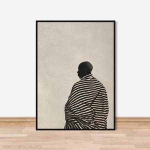 以下が含まれることがあります： 白黒のアートプリント。縞模様の衣服を着た人物のシルエットが描かれています。人物は後ろ姿で、ニュートラルな背景に配置されています。アートワークは黒いフレームに入っています。
