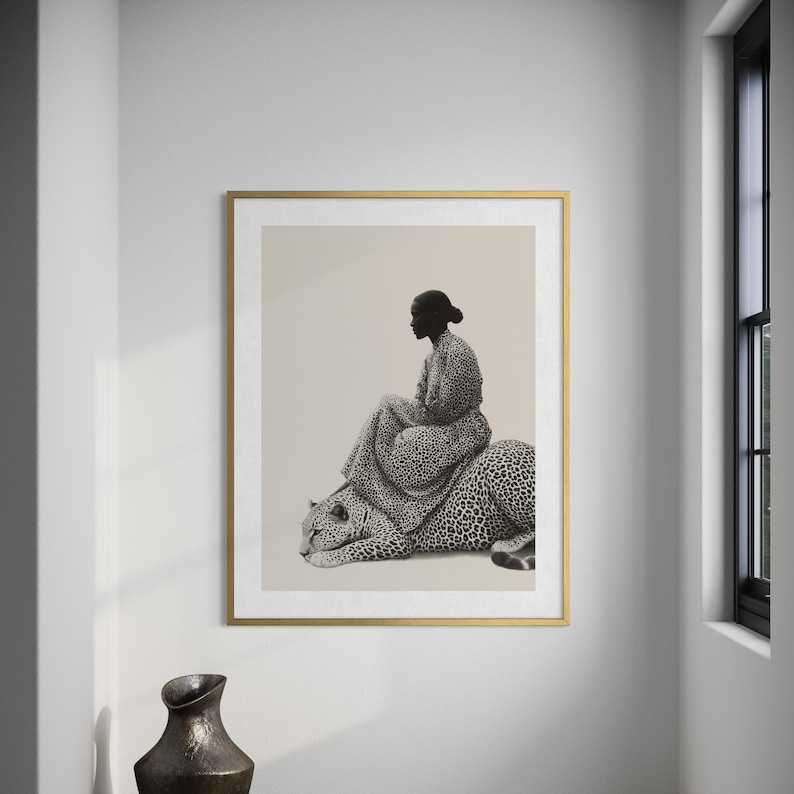 May include: A framed art print featuring a woman seated on a leopard. The woman and leopard are depicted in a black and white spotted pattern. The artwork is set against a neutral background and framed in gold.