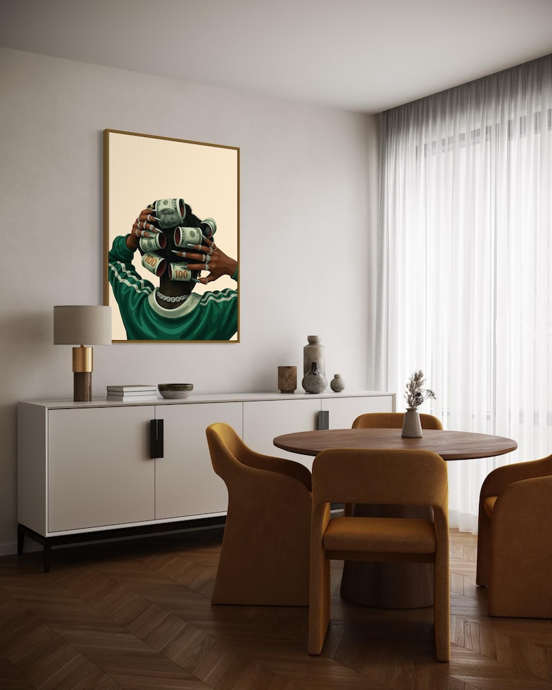 May include: A framed art print depicts a person with dollar bills rolled into curlers. The person wears a green and white track suit and a silver chain. The artwork hangs in a dining room with a white sideboard, round table, and mustard-colored chairs.