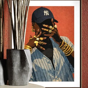 May include: Framed art print featuring a person wearing a navy blue baseball cap with a white "NY" logo, gold jewelry, and a blue and white striped shirt. The artwork has a red background and is displayed in a black frame.