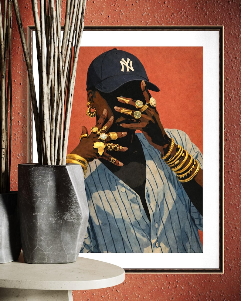 May include: Framed art print featuring a person wearing a navy blue baseball cap with a white "NY" logo, gold jewelry, and a blue and white striped shirt. The artwork has a red background and is displayed in a black frame.