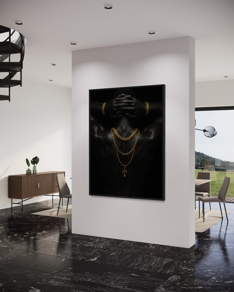 May include: A framed art print featuring a black and white image of a person's back, adorned with gold jewelry. The person's hands are behind their head, and gold chains and a pendant are visible. The artwork is displayed in a modern interior setting.