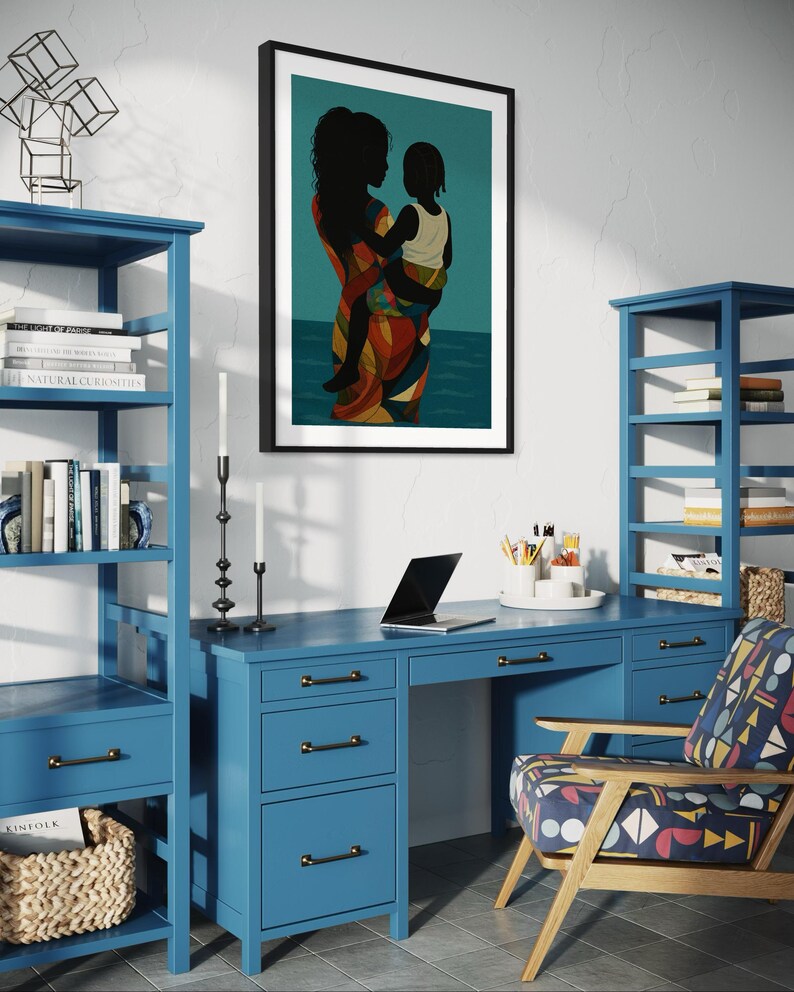 May include: A framed art print depicting a mother and child in silhouette, set against a teal background. The mother wears a colorful patterned dress. The print hangs above a blue desk and bookshelves, creating a home office setting.