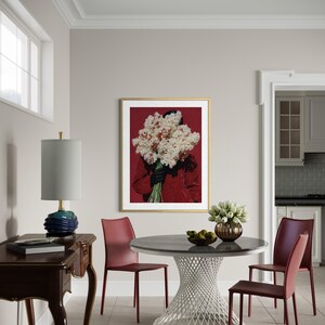 May include: A dining room scene featuring a round table with a white, latticework base and a dark gray top. Burgundy chairs surround the table. A framed artwork with a gold frame and a red background hangs on the wall. A blue lamp sits on a dark wood table.