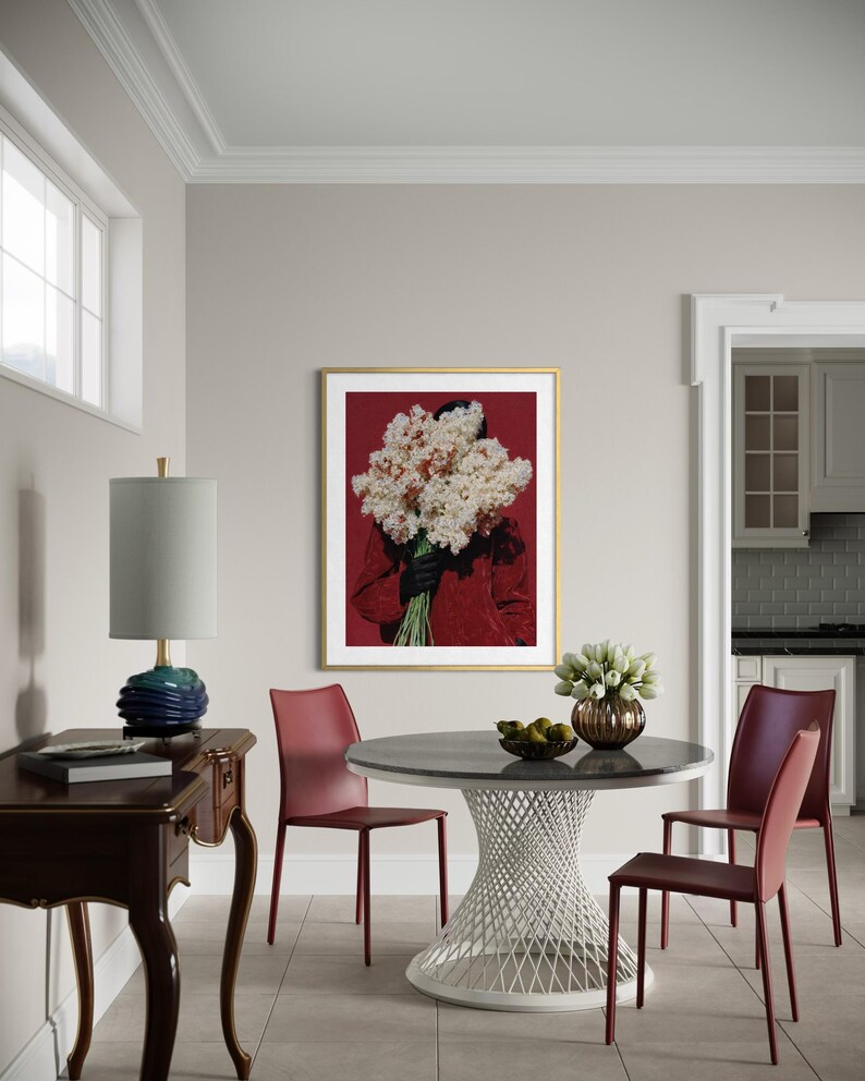 May include: A dining room scene featuring a round table with a white, latticework base and a dark gray top. Burgundy chairs surround the table. A framed artwork with a gold frame and a red background hangs on the wall. A blue lamp sits on a dark wood table.