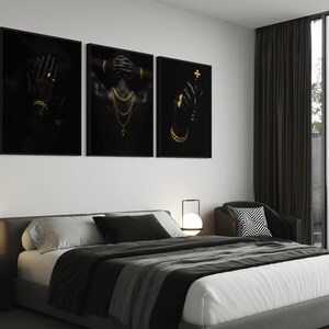 May include: Three framed black and gold art prints. The prints feature figures adorned with gold jewelry. The first print shows a hand with a ring and bracelet. The second print shows a figure with gold necklaces. The third print shows a hand holding a cross.