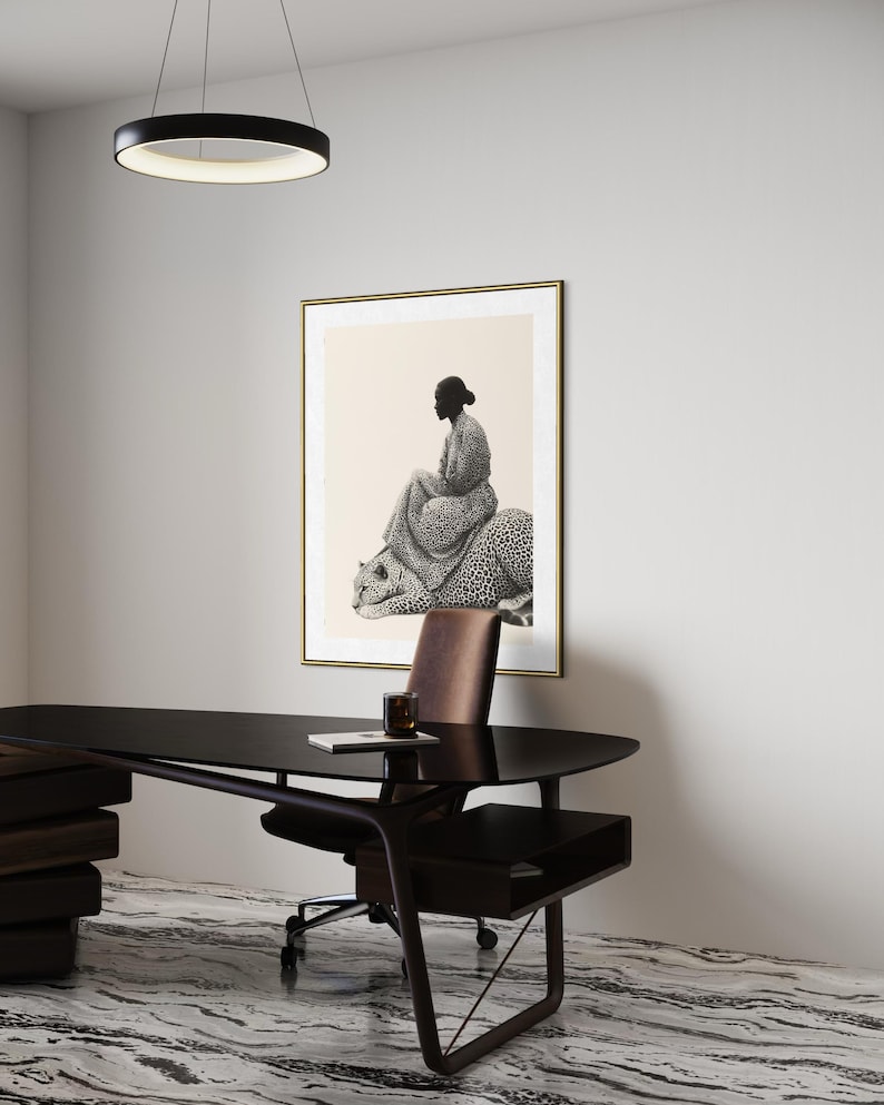 May include: An interior design scene featuring a framed artwork with a black and white illustration of a person seated on a leopard. A modern black desk, brown leather chair, and a circular light fixture are also visible.